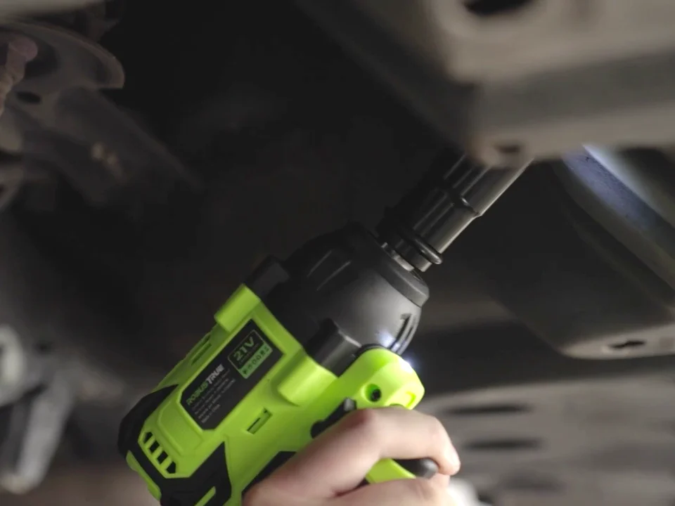 A Robustrue 21V impact wrench with its LED light on, reaching a bolt under a car